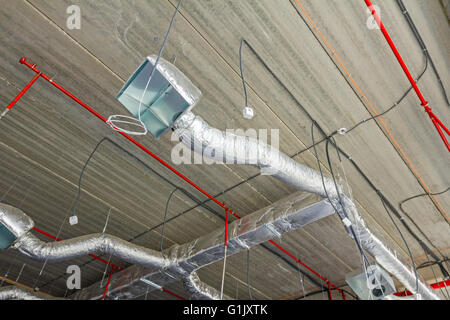 Ventilation pipes in silver insulation material hanging from the ceiling inside new building. Stock Photo