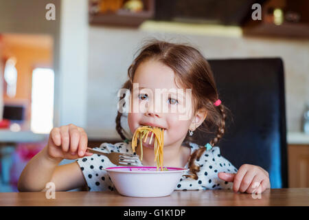 Little girl in the kitchen smiling, eating spaghetti Stock Photo