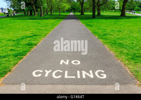 “No Cycling” warning written with white paint on tarmac pavement with visible  tree and grass at the background Stock Photo