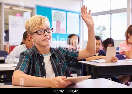 Boy with tablet raising his hand in elementary school class Stock Photo ...