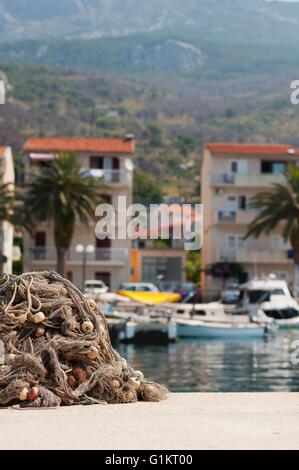 Pile of fishing nets with floats on a quay with blurred boats on background. Podgora, Croatia. Vertical photo Stock Photo