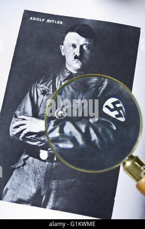 1930's B&W studio posed portrait photograph of Adolf Hitler in uniform with history researchers magnifying glass viewing detail incl. swastika motif Stock Photo