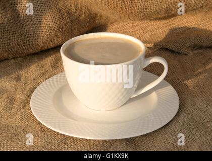 A cup of coffee bathed in evening sunlight on a Hessian background Stock Photo