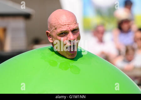 A children's performer pushes his head out of a large green inflatable balloon. Stock Photo