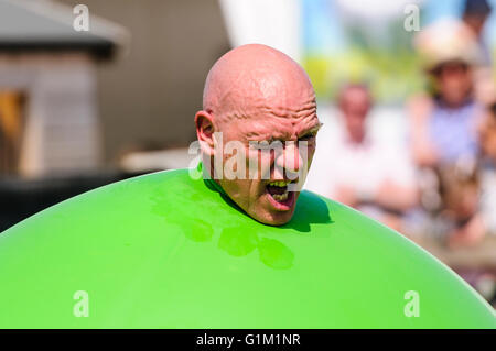 A children's performer pushes his head out of a large green inflatable balloon. Stock Photo