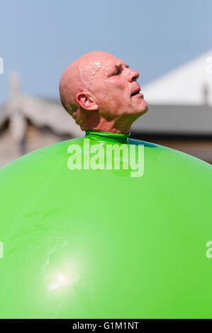 A children's performer pushes his head out of a large green inflatable balloon. Stock Photo