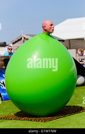 A children's performer pushes his head out of a large green inflatable balloon. Stock Photo