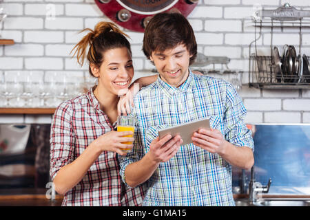 Happy young couple drinking orange juice and using tablet on the kitchen together Stock Photo