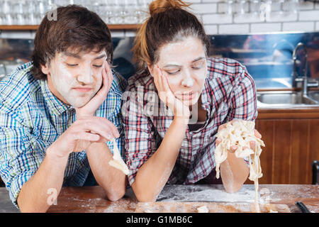 Sad bored young couple with flour on their faces kneading dough on the kitchen Stock Photo