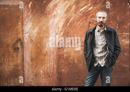 Outdoor portrait of young bearded Asian man in casual clothes on rusted urban grungy metal wall background Stock Photo