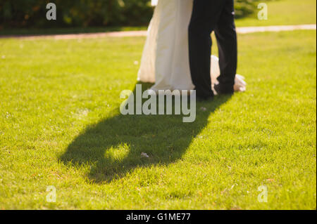 Shadow of couple kissing on the green grass. Bride and groom embracing. Long shadow on grass. Wedding picture at sunset. Stock Photo