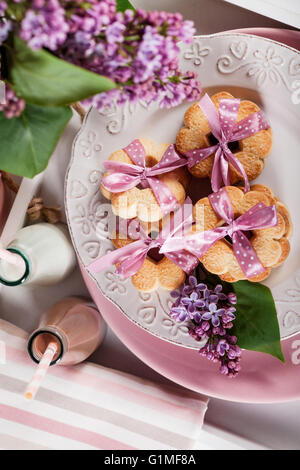 Cookies with pink ribbons on a white plate with lilac flowers and chocolate milkshake Stock Photo