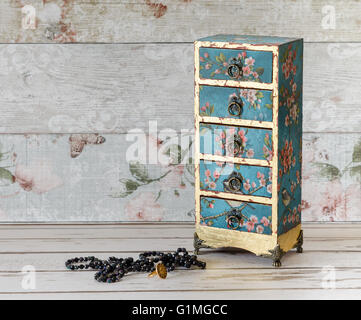 A beautiful handmade decoupaged jewelley box in a mini chest of drawers design on a rustic shabby chic background Stock Photo