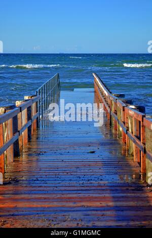 Small wooden Sea bridge on  the Baltic Sea coast of Germany, overrun by waves. Blue Sky and Blue Water. Stock Photo