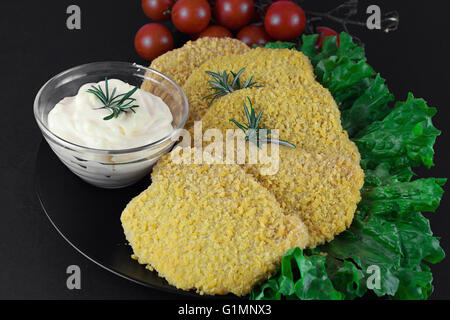 Chicken cutlet as known as Milanese with green salad, tomato ciliegino and mayo on complex background, on black background Stock Photo