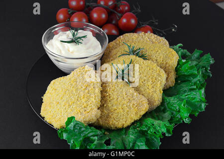Chicken cutlet as known as Milanese with green salad, tomato ciliegino and mayo on complex background, on black background Stock Photo