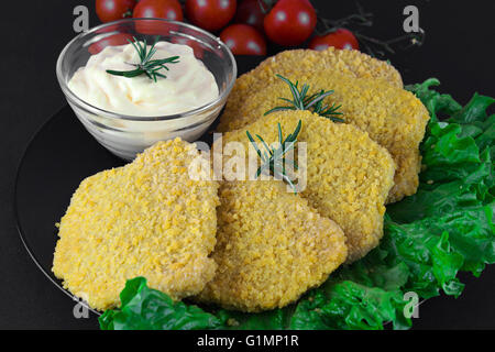 Chicken cutlet as known as Milanese with green salad, tomato ciliegino and mayo on complex background, on black background Stock Photo