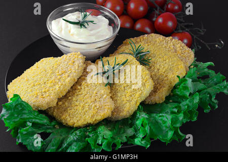 Chicken cutlet as known as Milanese with green salad, tomato ciliegino and mayo on complex background, on black background Stock Photo