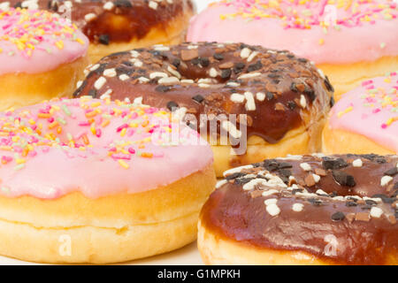 Rows of chocolate and pink iced doughnuts with sprinkles on an isolated white background. Stock Photo