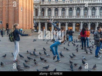 young tourists playing with / feeding pigeons on Piazza San Marco, Venice Stock Photo