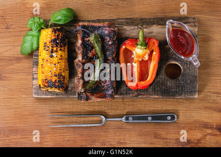 BBQ grilled pork ribs, corn, green chili and red bell pepper, served on wooden chopping board with barbecue sauce, fresh basil a Stock Photo