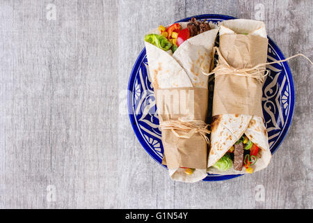 Mexican style dinner. Two papered tortillas burrito with beef and vegetables served on blue ornamental ceramic plate over white Stock Photo