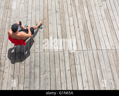 Young man sunbathing with beer in hand on wooden decking on beach Stock Photo