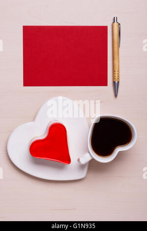 Coffee cup jelly cake in form of heart and red paper blank with pen on wooden surface, top view copy space for text Stock Photo