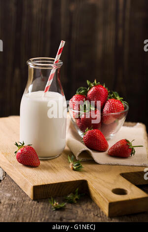 Dark still life with milk and strawberry on rough wood Stock Photo
