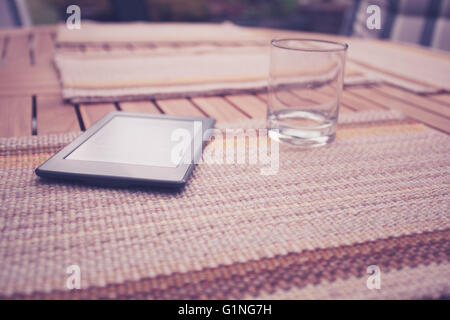 A digital tablet and an empty glass on a table outside in summer Stock Photo