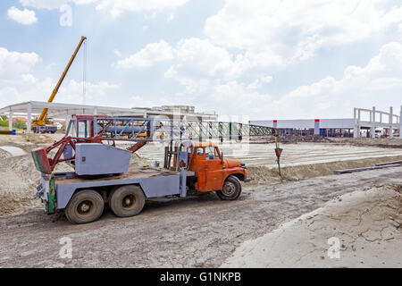 Rusty old mobile crane is parked at construction site. Landscape transform into urban area. Stock Photo