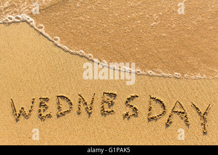 Wednesday - inscription by hand on a light-golden beach sand. Stock Photo