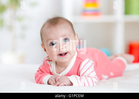 Very happy laughing baby in pink clothes lying on his belly. Infant looking straight at the camera Stock Photo