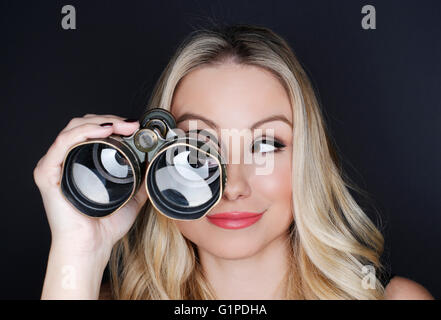 Beautiful blonde looking through old binoculars on black background Stock Photo