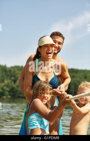Family and kids having fun playing tug of war on their summer holidays Stock Photo