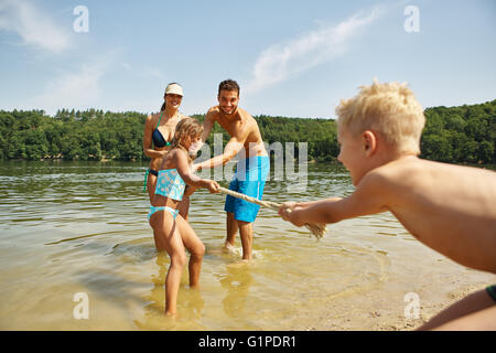 Happy family pulling the rope at the lake in summer Stock Photo