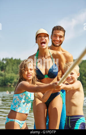 Family and kids having fun playing tug of war in the summer at the lake Stock Photo