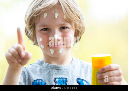 Little boy puts himself sunscreen on the face, sun protection, Stock Photo