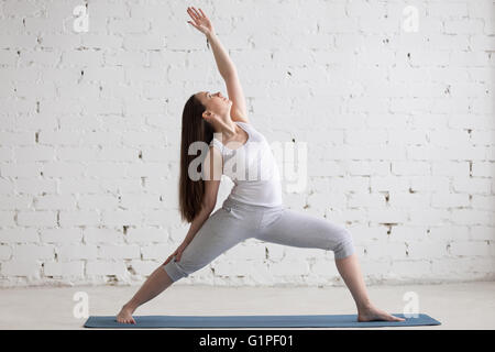 Attractive cheerful young woman working out indoors. Beautiful model doing exercises on blue mat in room with white walls Stock Photo