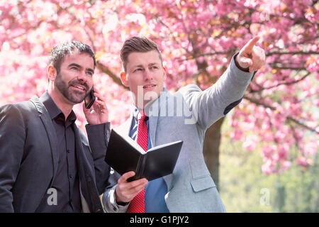 two businessmen standing in park with book and phone Stock Photo