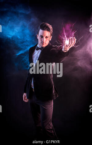 Portrait of young handsome magician in elegant suit and bow-tie holding lightning in hand Stock Photo