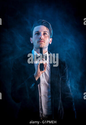 Portrait of young handsome man in elegant smoking committing suicide with gun on neck Stock Photo