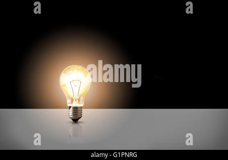 One incandescent light bulb on white table with black background. Front view. Horizontal composition Stock Photo