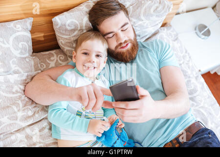 Top view of dad and son lying on bed and using cell phone together Stock Photo