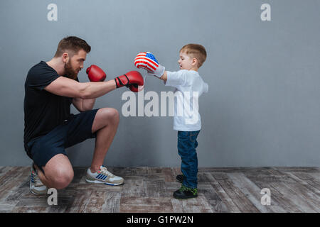 Father and little son working out in boxing gloves together over grey background Stock Photo