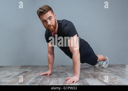 Serious bearded young sportsman doing plank core exercise over grey background Stock Photo