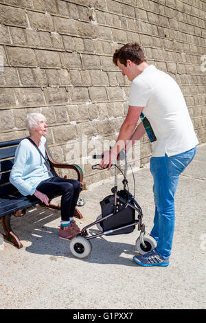 An Elderly Disabled Woman Getting Up From A Bench, Helped By Her Grandson, Brighton, Sussex, UK Stock Photo