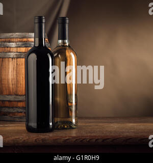 Red and white wine bottles and wooden barrel on the cellar table, wine making still life Stock Photo