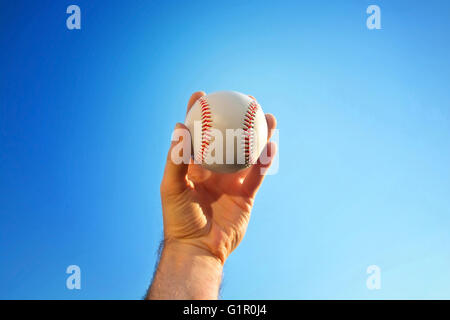 Baseball game. Baseball ball holding by hand against blue clean sky. Stock Photo