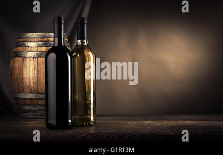 Red and white wine bottles and wooden barrel on the cellar table, wine making still life Stock Photo